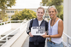 photo of two young women smiling to the camera holding a sign with the words welcome week at ISEP